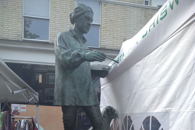 The statue of the artist and his dog crowded by the market stall 